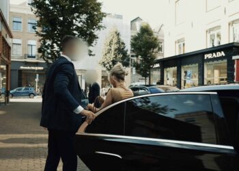 Bodyguard services in Amsterdam | Infinite Risks | A luxurious car parked on a city street with a well-dressed man assisting a woman entering the vehicle.