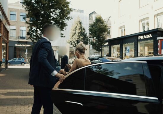 Persoonsbeveiliging in Amsterdam | Infinite Risks | Een luxe auto in de stad met een man in een pak die een vrouw helpt instappen.